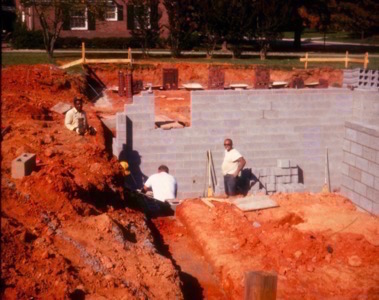 three men construction a basement wall using concrete blocks